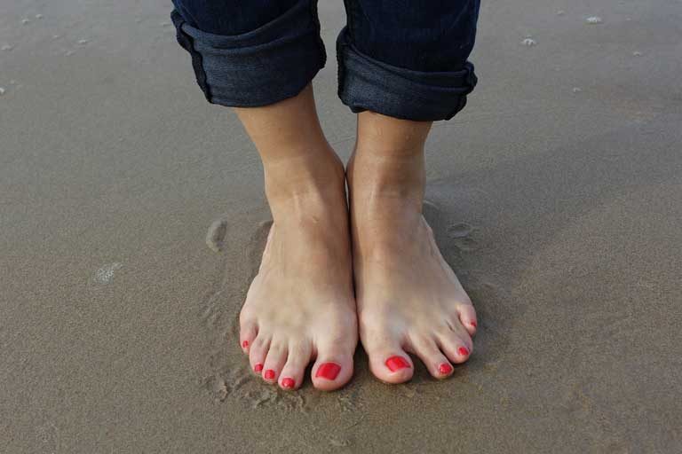Frauenfuesse mit rot lackierten Naegeln am Strand